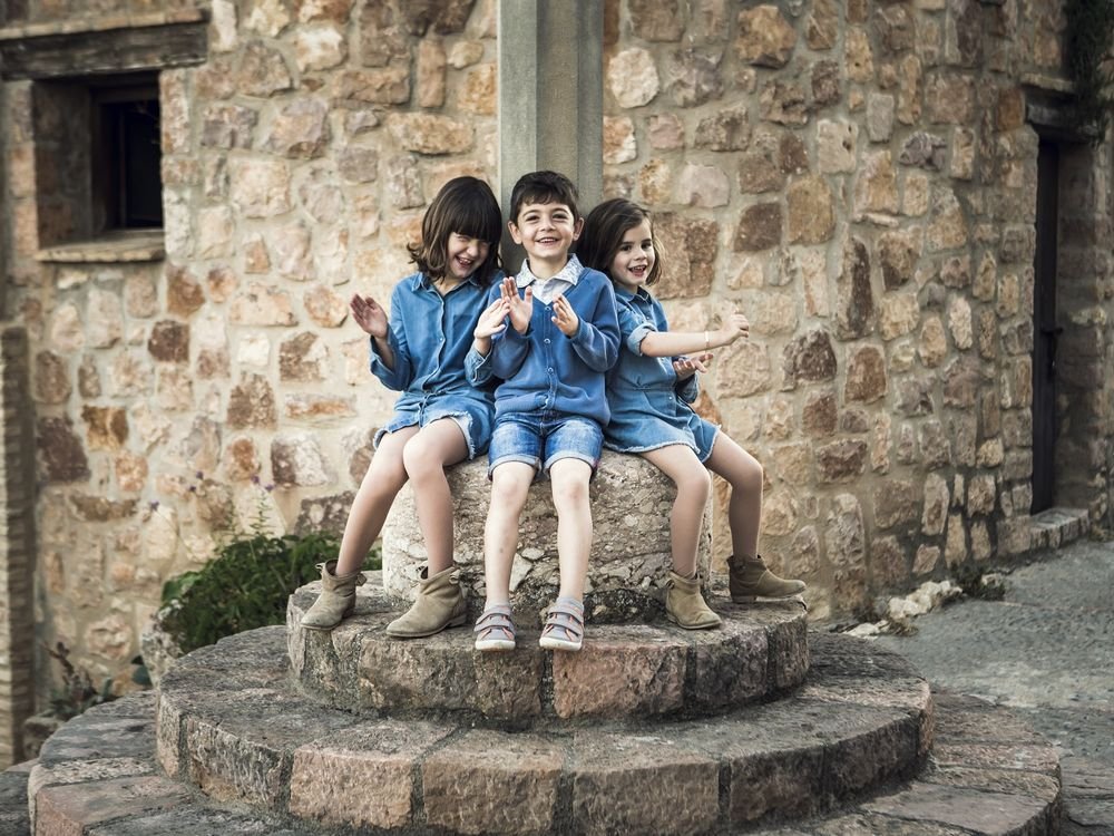 Tres niños sentados en una piedra de molino en un pueblo del Somontano